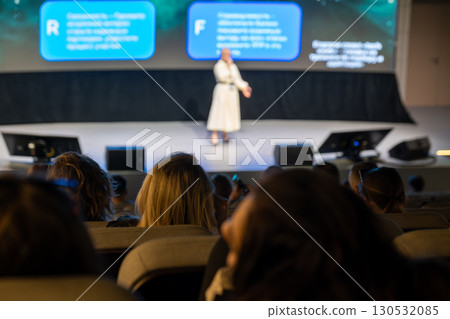 Speaker presenting at conference viewed from audience perspective in modern auditorium 130532085