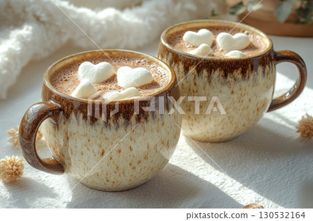 Two ceramic cups filled with hot chocolate topped with heart-shaped marshmallows sit on a cozy surface. Concept of warmth and comfort. For social media posts on cozy drinks. 130532164