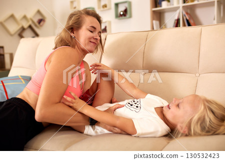 Mother and daughter laughing together on a cozy sofa at home Mother and daughter laughing together on a cozy sofa at home 130532423