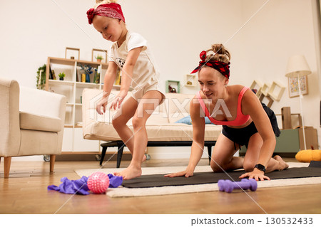 Mother and daughter exercising together on a yoga mat indoors Mother and daughter exercising together on a yoga mat indoors 130532433