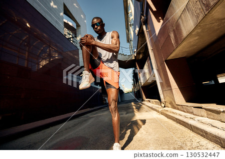 Young athlete stretching in an urban environment with modern architecture Young athlete stretching in an urban environment with modern architecture 130532447