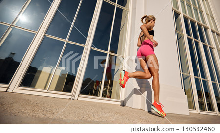 Athletic woman jogging outdoors against a building in sunny weather 130532460