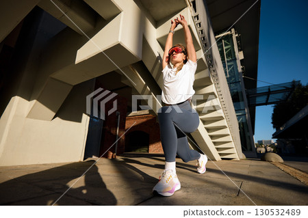 Woman performing stretch lunge exercise outdoors in a modern urban environment Woman performing stretch lunge exercise outdoors in a modern urban environment 130532489