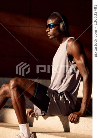 Man Relaxing on Steps Wearing Sportswear and Headphones in Natural Sunlight Man Relaxing on Steps Wearing Sportswear and Headphones in Natural Sunlight 130532493