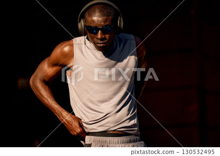 Athletic man in sporty attire listening to music during intense workout. Athletic man in sporty attire listening to music during intense workout. 130532495