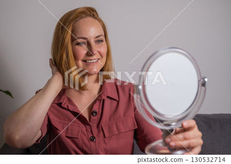 Smiling, happy middle age woman looking at mirror touching her skin, aging, skin care 130532714