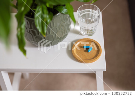 Blue capsule pills with glass of water on the table, lifestyle shot 130532732