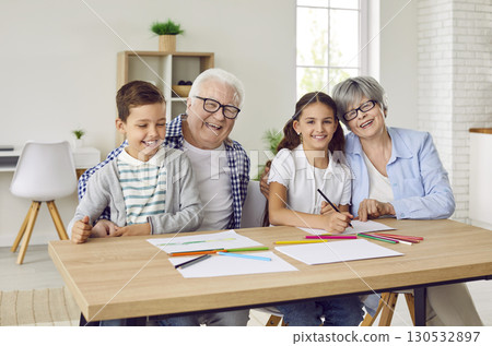 Happy, smiling grandparents and children sitting at table and drawing with pencils Happy, smiling grandparents and children sitting at table and drawing with pencils 130532897