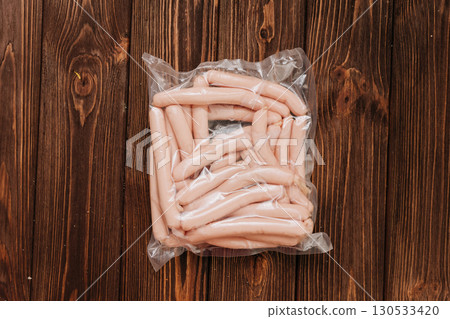 Vacuum packed chicken sausages on wooden table with tomatoes and salt in background 130533420