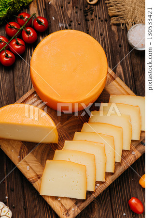 Round cheese wheel and sliced cheese on wooden board with rustic food ingredients 130533421