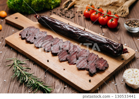 Sliced dry sausage on rustic wooden board with spices and tomatoes, top view Sliced dry sausage on rustic wooden board with spices and tomatoes, top view 130533441