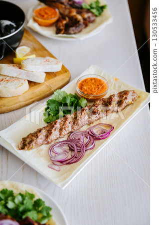 Traditional kebab with herbs, red onion and sauce on lavash, served on a white plate Traditional kebab with herbs, red onion and sauce on lavash, served on a white plate 130533456