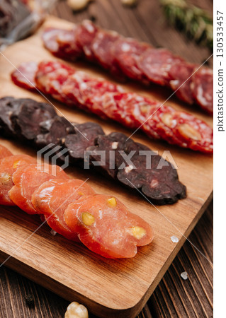 Close-up of gourmet sliced sausage with nuts on wooden board, traditional cured meat snack 130533457