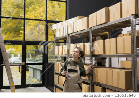 Employee focused on parcel preparation and logistics with list on clipboard, product handling and shipment service for e-commerce, drop shipping and express delivery. In house operations. 130533646