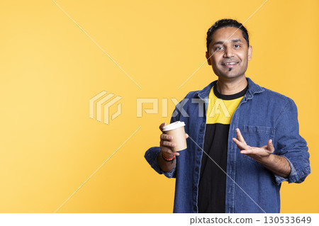 Indian male model feeling energized after drinking a cup of coffee from paper disposable container against studio background. Young adult enjoying cappuccino on a coffee break. 130533649