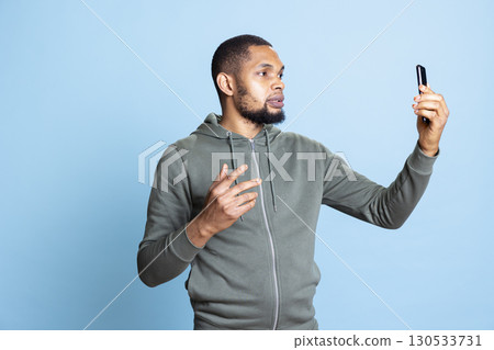 Joyful relaxed man having entertaining conversation with friends during teleconference meeting on a smartphone in studio. Happy person having fun interacting with pals during online videocall. 130533731
