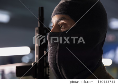 Close up of terrorist wearing mask holding rifle, prepared to start guerilla warfare operation against enemies. Rebel forces insurgent with weapon in hidden base starting offensive against opponents Close up of terrorist wearing mask holding rifle, prepared to start guerilla warfare operation against enemies. Rebel forces insurgent with weapon in hidden base starting offensive against opponents 130533743