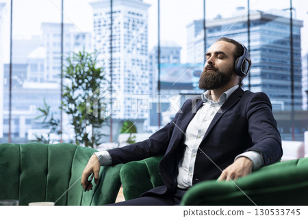 Director pauses for a moment of calmness listening to meditation sounds through his headphones, self care at the office. Mindfulness essential for leadership and global business success. Director pauses for a moment of calmness listening to meditation sounds through his headphones, self care at the office. Mindfulness essential for leadership and global business success. 130533745