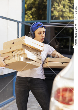 Takeaway delivery worker parking the car and bringing pizza boxes to client at the front door, delivering a massive fast food order. Female courier ensuring an express five star service. 130533829