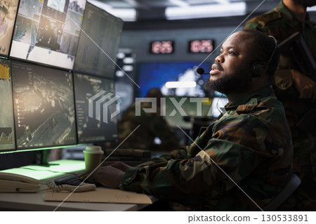 Officer responsible for air defense relaying instructions to squadrons patrolling over borders using headphones microphone. African american military intelligence agent communicating with troops Officer responsible for air defense relaying instructions to squadrons patrolling over borders using headphones microphone. African american military intelligence agent communicating with troops 130533891