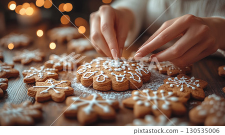Close-up hand placing Christmas tree-shaped gingerbread cookie white icing among snowflake cookies. 130535006