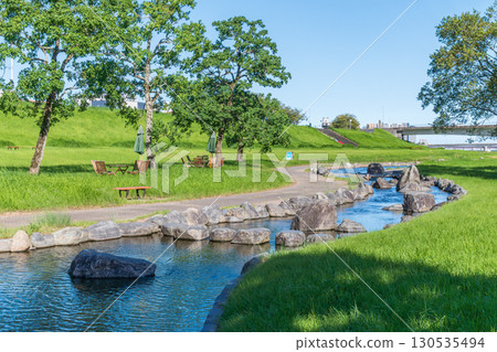 鬱鬱蔥蔥的大淀川濱水公園裡，沿著水邊擺放桌椅 130535494