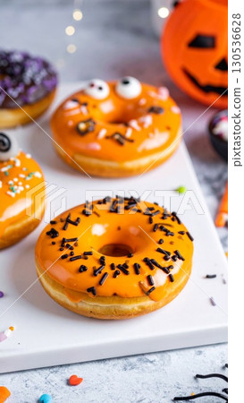 Delicious Orange Halloween Donuts with Black Sprinkles on Marble Surface and Festive Decoration 130536628
