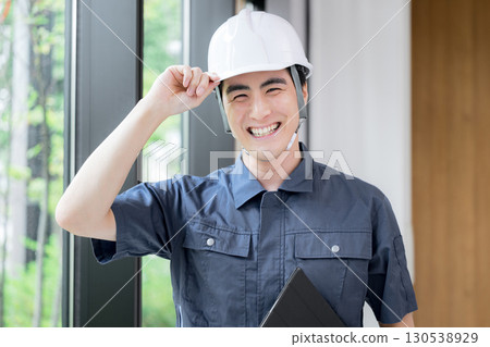 A man wearing work clothes and a helmet looking at the camera, maintaining buildings, etc. 130538929