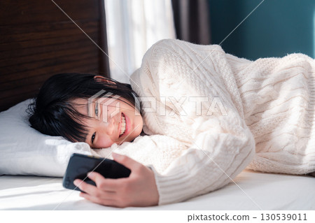 An adolescent girl lying on the bed and using a smartphone 130539011