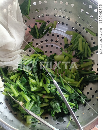 Steamed green vegetable stems and leaves in metal steamer with tongs, fresh and vibrant, simple healthy meal preparation 130540866