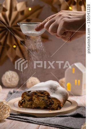 Christmas Stollen with falling sugar powder in Christmas lights and decoration. Traditional sweet fruit loaf with icing sugar festive pastry dessert. Holiday baking food 130541228