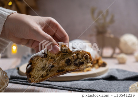 Woman taking slice of Traditional German Christmas stollen cake in background of handmade festive decor. Winter holiday treats. Vegan baking recipe 130541229