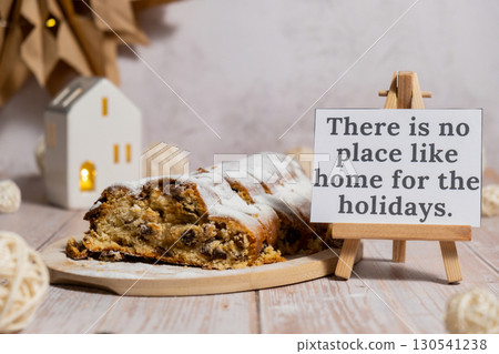 Paper note with text THERE IS NO PLACE LIKE HOME FOR THE HOLIDAYS. Homemade Christmas traditional cake pie with marzipan nuts and dried fruits pastry dessert stollen. Winter holidays season atmosphere Paper note with text THERE IS NO PLACE LIKE HOME FOR THE HOLIDAYS. Homemade Christmas traditional cake pie with marzipan nuts and dried fruits pastry dessert stollen. Winter holidays season atmosphere 130541238