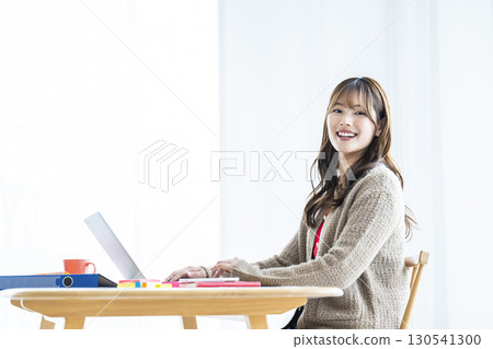 Young woman using laptop, looking at camera, smiling 130541300