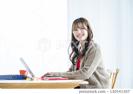 年輕女子使用筆記型電腦，看著相機，微笑 130541307