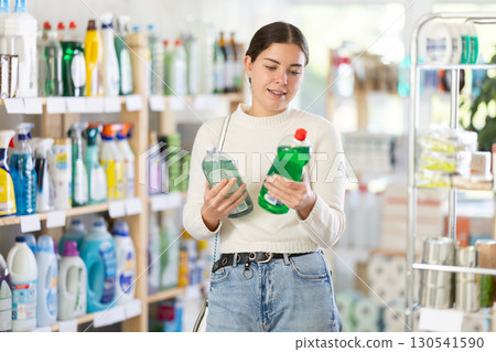 Girl housewife in household store examines package, chooses dishwashing Girl housewife in household store examines package, chooses dishwashing 130541590