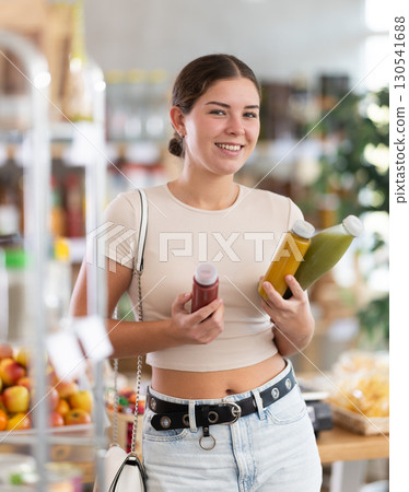 European smiling girl hold bottle, choose and buy smoothie in store European smiling girl hold bottle, choose and buy smoothie in store 130541688