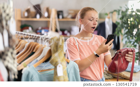 Surprised teenage girl scanning QR-code on handbag in clothing store Surprised teenage girl scanning QR-code on handbag in clothing store 130541719