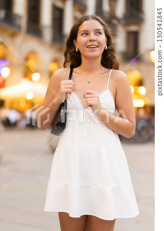 In evening, young smiling girl walks along city street Placa Real In evening, young smiling girl walks along city street Placa Real 130541845