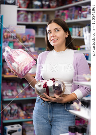 Smiling woman holds two sets of skin and haircare products in her hands during purchases in cosmetic boutique 130541965
