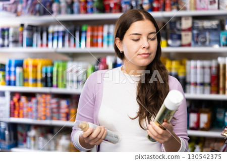 Young brunette selecting and comparing two hair styiling spray 130542375