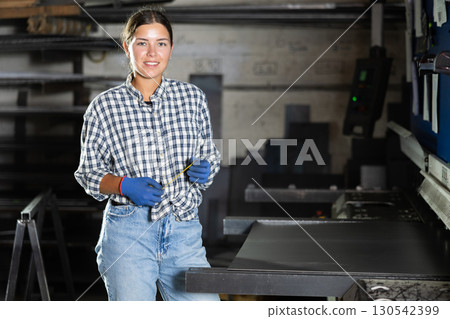 Young female technician with tape measure posing in metal workshop Young female technician with tape measure posing in metal workshop 130542399