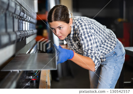 Young woman bends sheet of metal under pressure 130542557
