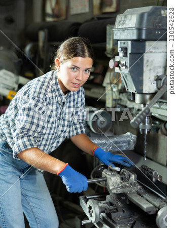 Young workwoman operating drill press in metal workshop 130542628