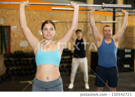 Motivated CrossFit female athlete lifting heavy body bar or barbell during group training in gym. Functional training concept. 130542721