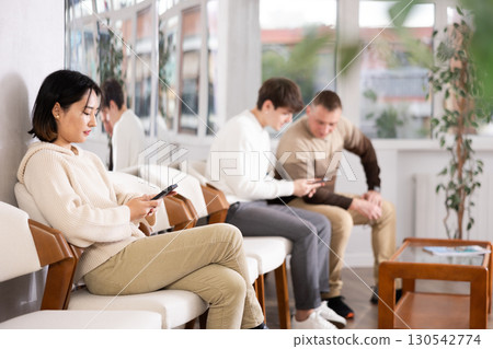 Girl sits in lobby of employment office, waiting for interview or conversation with career consultant. Watches news on Internet via smartphone Girl sits in lobby of employment office, waiting for interview or conversation with career consultant. Watches news on Internet via smartphone 130542774