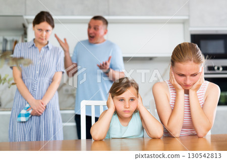 Frightened and frowning children sit at kitchen table during mom and dad quarrel. Frightened and frowning children sit at kitchen table during mom and dad quarrel. 130542813