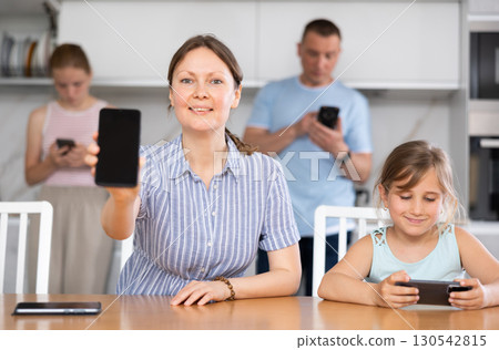 Mom showing the screen of her phone. Children and husband typing on smartphone screen 130542815