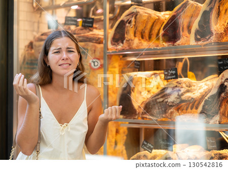 Outraged woman customer stands near shop window with dried beef ribs 130542816