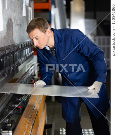Adult man bends metal sheet under pressure 130542860
